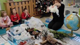 Dzieci siedzą w kole. Prowadząca warsztaty kobieta wyjaśnia jak powstaje śnieg.