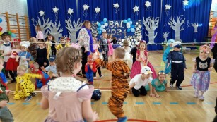 Bal karnawałowy. Sala gimnastyczna udekorowana bibułą, balonami i srebrnymi ozdobami. Dzieci przebrane w stroje karnawałowe uczestniczą w zabawie tanecznej.