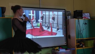 Dzieci oglądają prezentację. Baletnica opowiada opowiada o zajęciach tanecznych związanych z tańcem baletowym