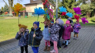Dzieci z kolorowymi kwiatami z bibuły i marzanną maszerują w wiosennym korowodzie