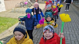 Dzieci z kolorowymi kwiatami z bibuły idą chodnikiem
