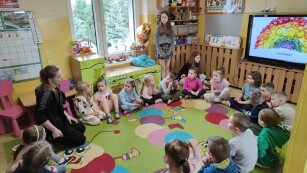 Dzieci siedzą w kole na dywanie. Słuchają siedzącej z nimi nauczycielki