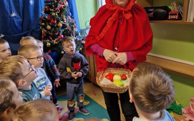 Nauczycielka przebrana za Czerwonego Kapturka rozmawia ze stojącymi przed nią  dziećmi