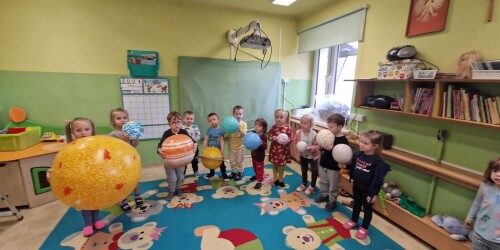 Dzieci trzymają w rękach pompowane piłki różnej wielkości i różnego koloru przedstawiające planety.