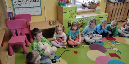 Dzieci siedzą w kole. Chłopiec, podczas swojej wypowiedzi, trzyma misia na kolanach.