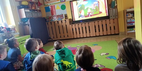 Dzieci siedzą przed ekranem tablicy multimedialnej. Oglądają przedstawienie 