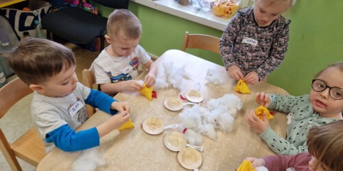 Dzieci siedzą przy stolikach, wypełniają watą materiałowe kurczaki