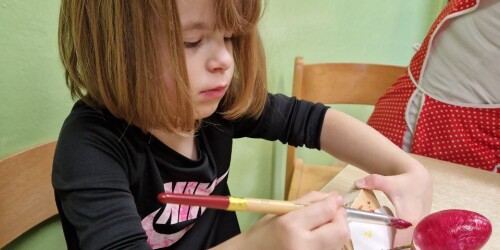 Dziewczynka maluje pędzelkiem styropianowe jaj ka kolorową farbą