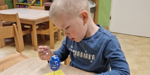 Chłopiec maluje pędzelkiem styropianowe jaj ka kolorową farbą
