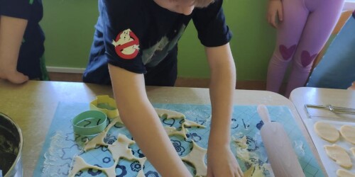 Dziecko wykrawa z rozwałkowanego ciasta foremką ciasteczka