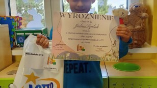 Uśmiechnięty chłopiec prezentuje dyplom i nagrody otrzymane w konkursie