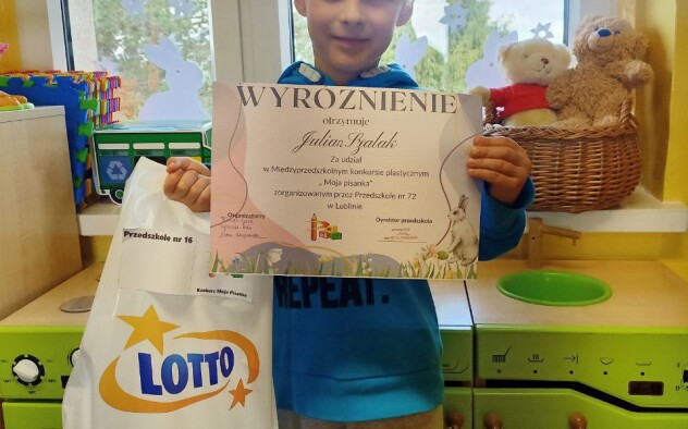 Uśmiechnięty chłopiec prezentuje dyplom i nagrody otrzymane w konkursie
